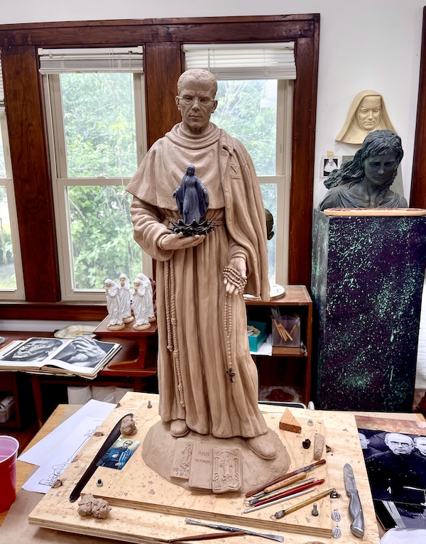 Clay sculpture of a priest in his robes holding a small Madonna statue.