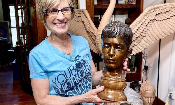 The Artist Sondra Jonson Cambridge NE holding a bronze bust of a young boy.