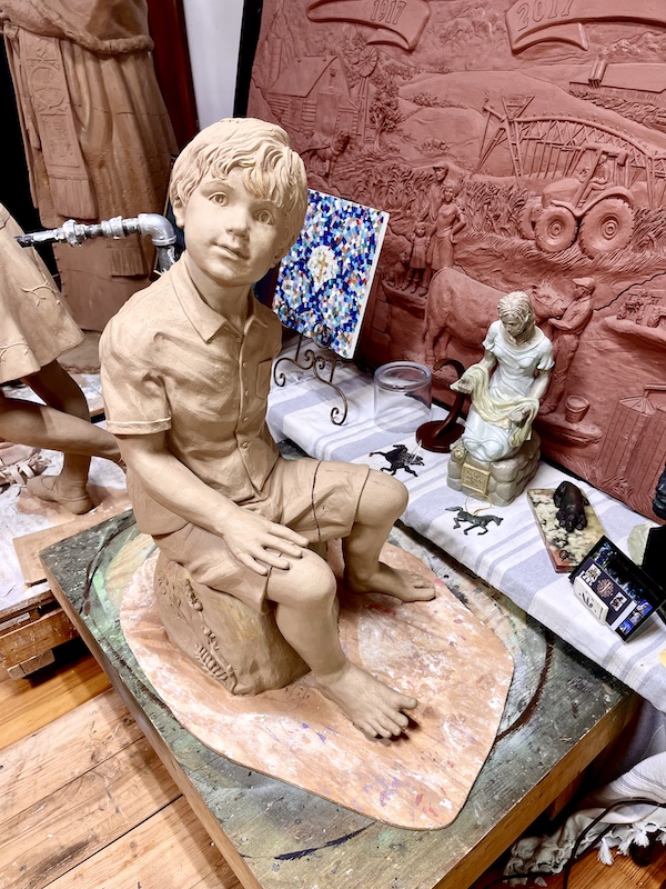 Clay sculpture of a young boy sitting on a tree stump by Artist Sondra Jonson Cambridge NE