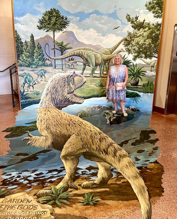 Me in a red white and blue dress standing in front of a painting of dinosaurs at Garden of the Gods