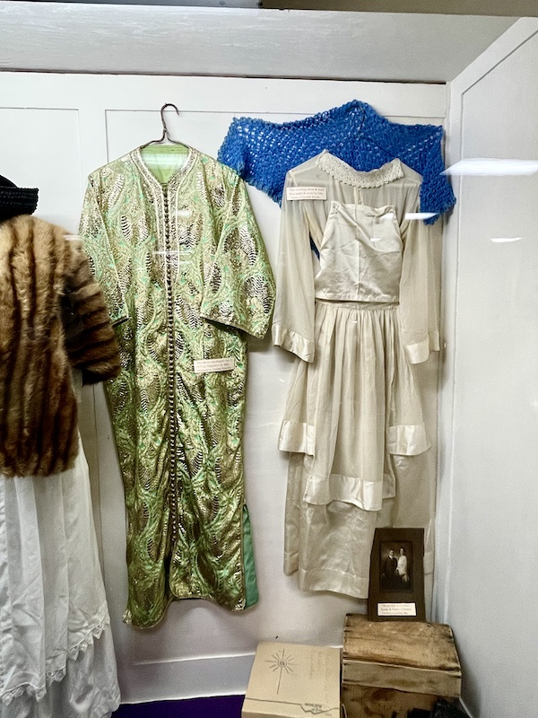Old fashioned white wedding gown, green kimono and white dress with sable stole hanging on wall at Nebraska's Cambridge Museum