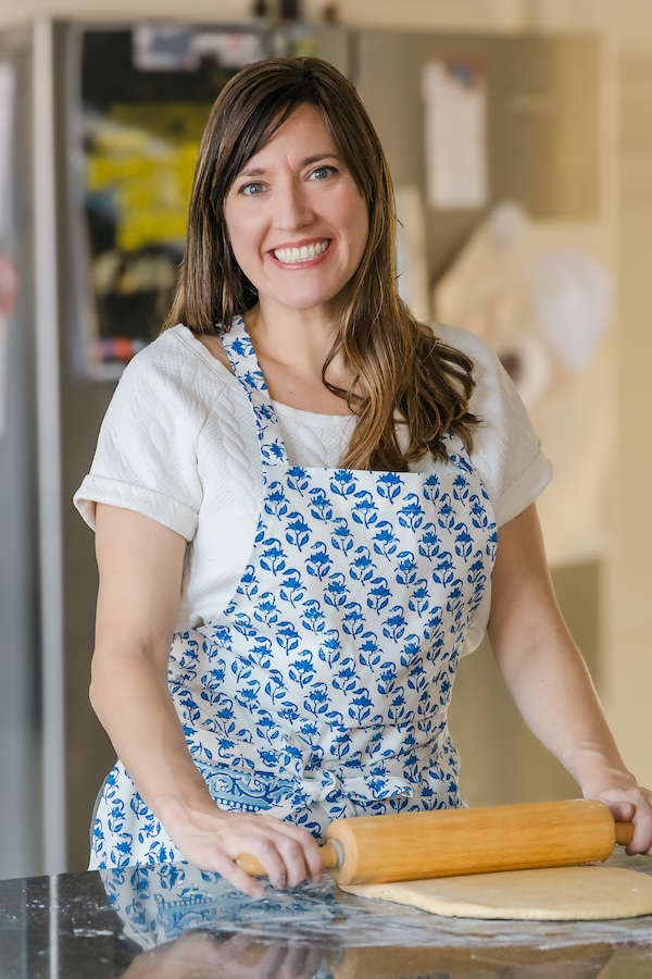 Woman in blue and white apron rolling dough is author of 30 Breads to Bake Before You Die