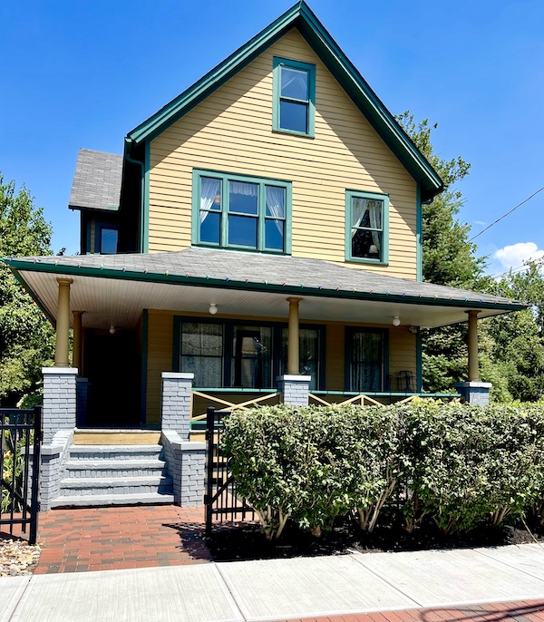 Yellow house with green trip and front porch with hedge is The Christmas Story House