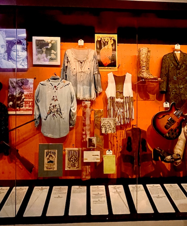 Fringed vests and other attire worn by Santana on display on an orange background at Rock and Roll Hall of Fame