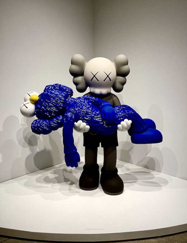 Sculpture of a blue whimsical figure being held by a black and gray whimsical figure on display at the Andy Warhol Museum Pittsburgh