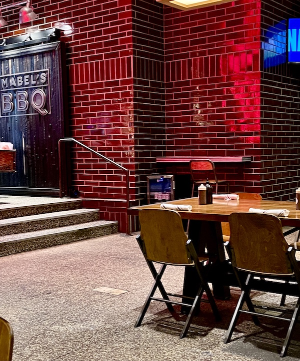 Red tiled walls, wood tables and chairs inside Michael Symon's Mabel's BBQ