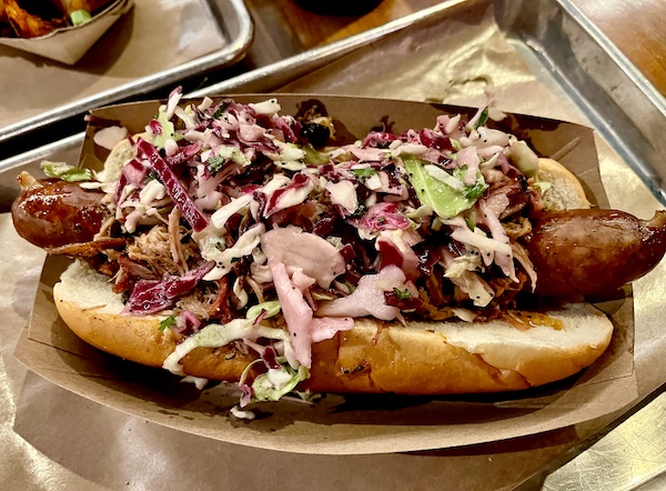 Plate with a hoagie roll filled with kielbasa pulled pork and slaw at Michael Symon's Mabel's BBQ