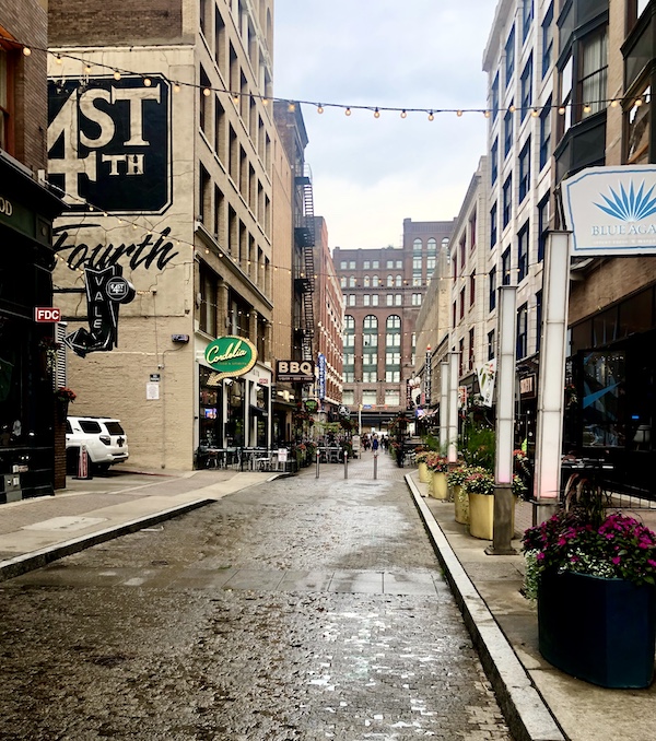 Narrow city street with buildings on each side and Michael Symon's Mabel's BBQ on left.
