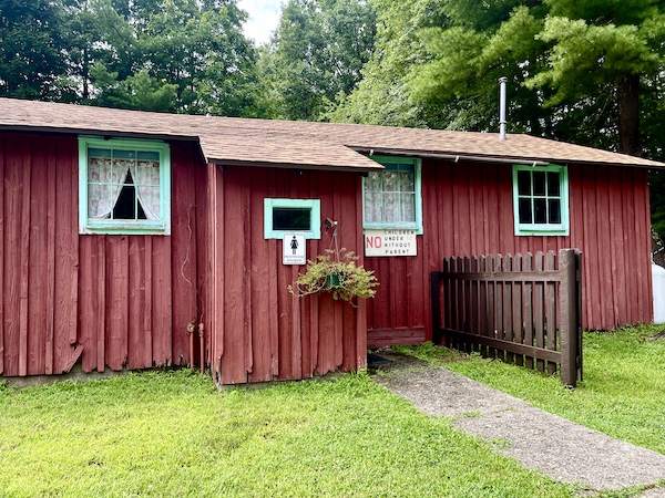 Old red wood building with turquoise trimmed windows , lawn and trees at our campground in Upstate New York