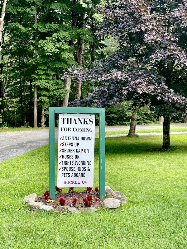 White sign with black lettering and green frame on lawn of campground in Upstate New York