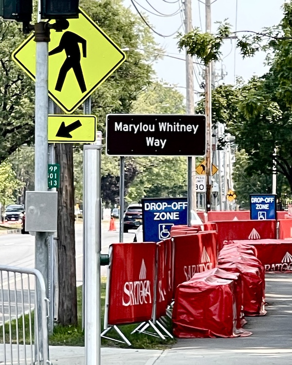 Street and walkway just outside Historic Saratoga Race Course with black street sign for Marylou Whitney Way