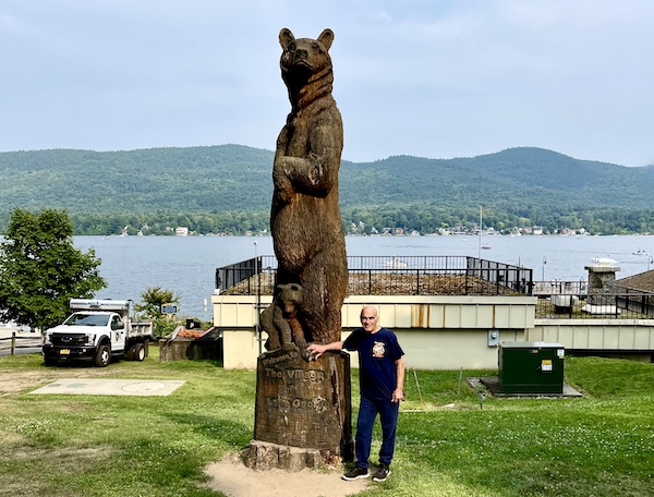 Enormous wood carving of a bear and cub with Steve standing next to it. behind is Lake George New York