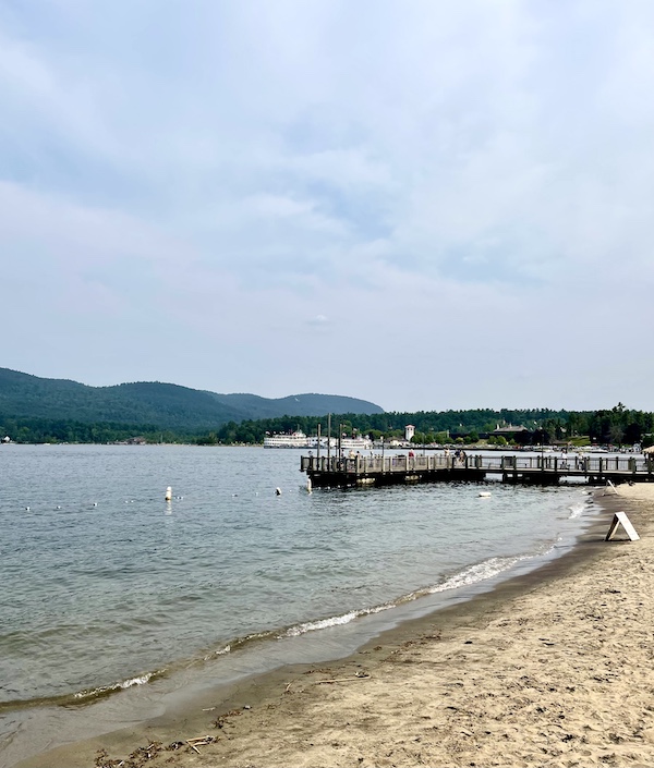 View of the beach at Lake George New York with steamboat in the distance.