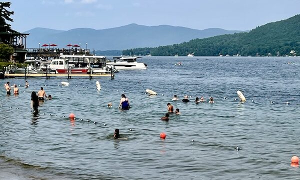 People swimming in Lake George New York with beach visible in foreground and the mountains in background