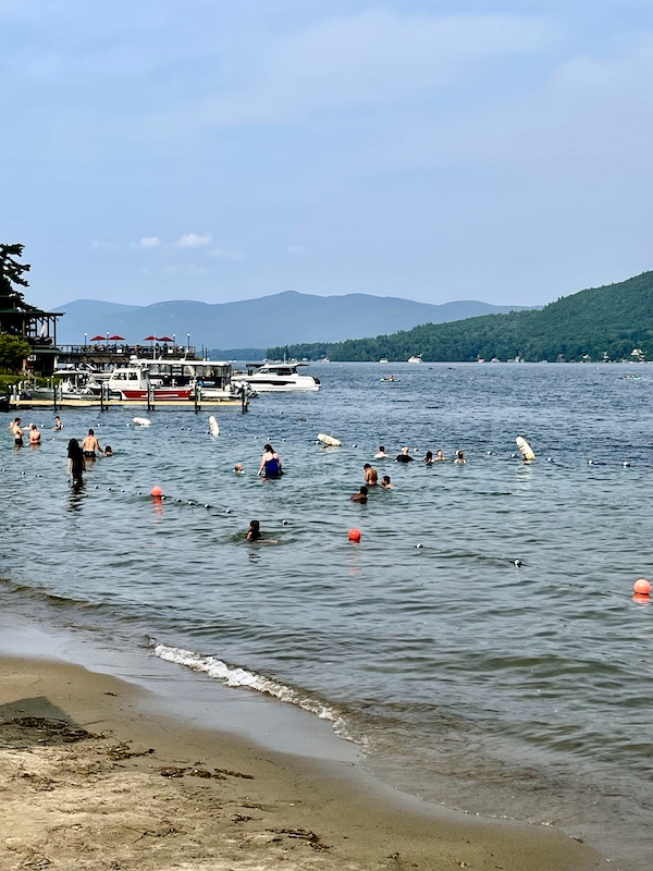 People swimming in Lake George New York with beach visible in foreground and the mountains in background
