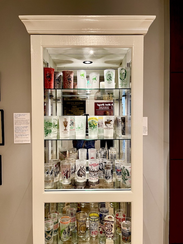 Painted display case with shelves holding assorted shot glasses at the National Museum of Racing and Hall of Fame