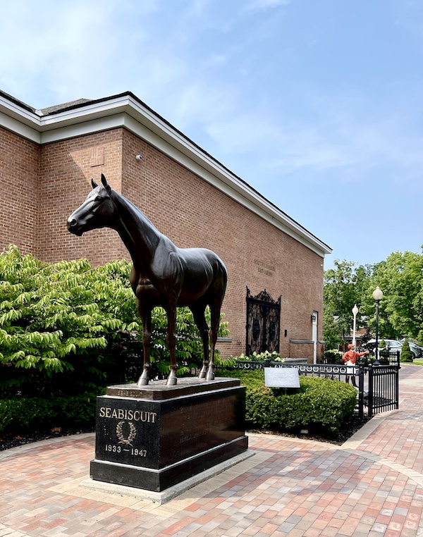 Bronze statue of horse Seabiscuit just outside the National Museum of Racing and Hall of Fame building on a patio of pavers.