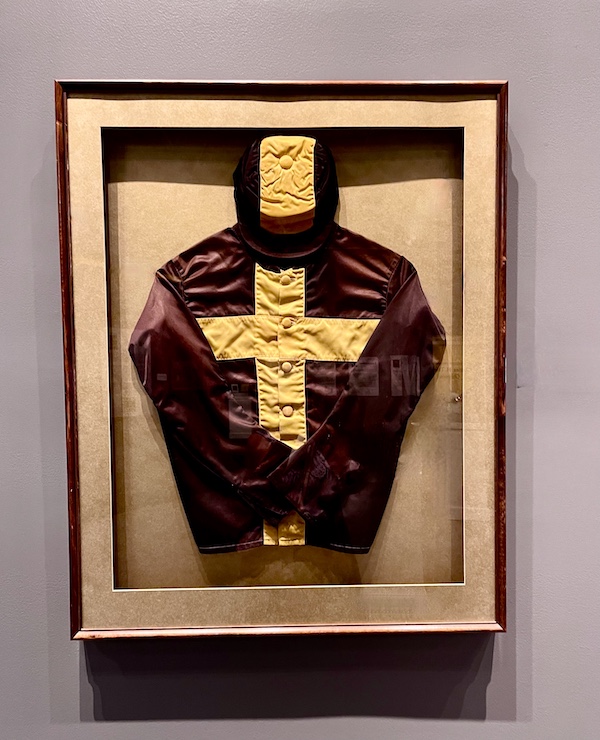Dark gray silk shirt with yellow cross in a display case at the National Museum of Racing and Hall of Fame