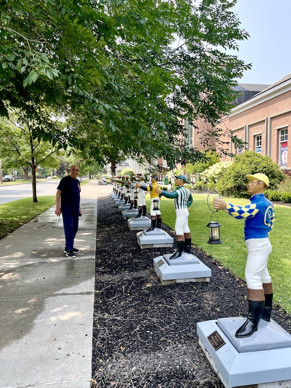 Steve on the sidewalk next to a row of colorful lawn jockeys at the National Museum of Racing and Hall of Fame
