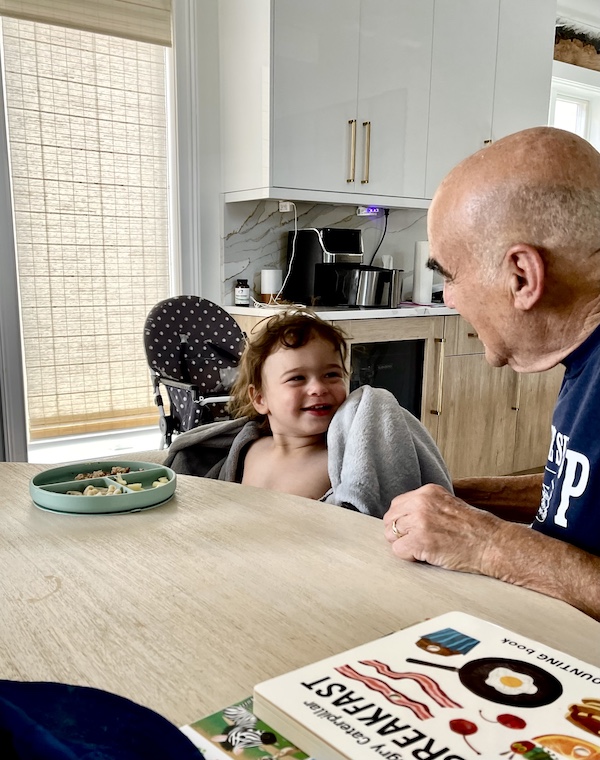 Toddler holding a blanket and Steve next to him at the table.