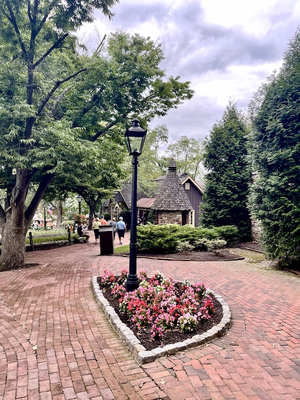 Red brick paver path with trees and flower beds lead to the Sand Sculptures Peddler's Village