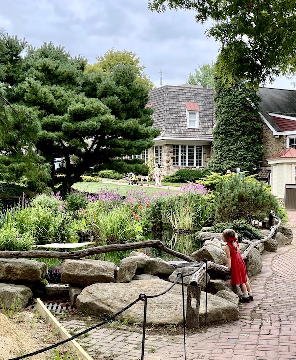 Little girl in red dress looking over rail at pond and flowering landscape