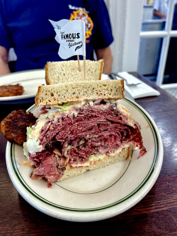 Cream plate with half a sandwich that includes rye bread pastrami piled high and coleslaw with Russian dressing.