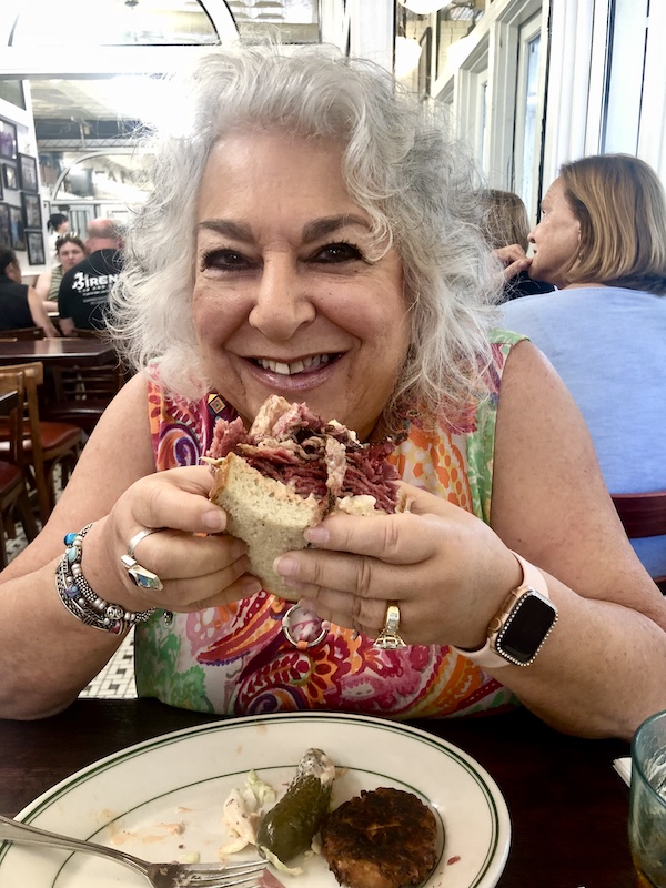 Woman with silver hair about to bite into a huge sandwich.