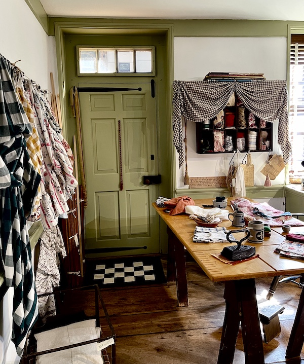 Fabric hanging on hooks on a wall, entry door and table seen while Visiting Betsy Ross' House