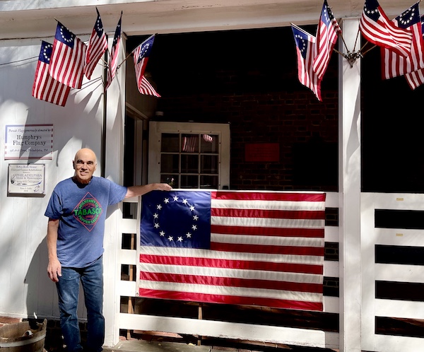 Steve standing by a fence with a replica of the first American flag draped on it.