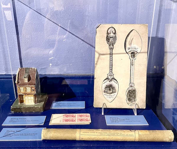 Drawings of spoons and a small Betsy Ross' House replica in a display case.