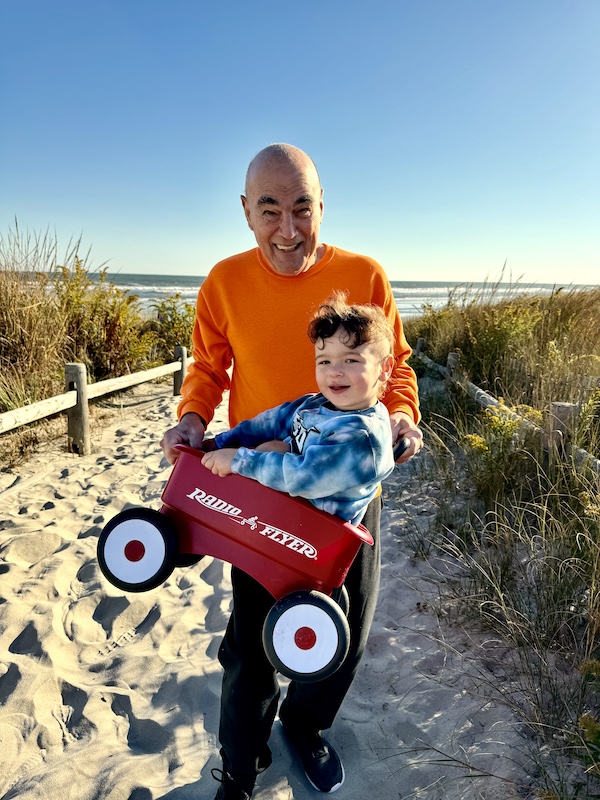 Steve in orange sweatshirt holding a red wagon with a toddler in it.
