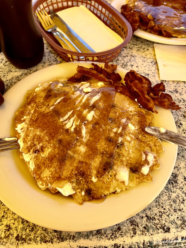 Pale yellow plate topped with blueberry pancakes with butter and syrup.