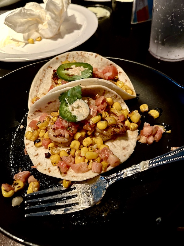 Pair of shrimp filled tacos on a black plate with a fork across the front edge at Basket lined with deli paper and filled with seasoned crinkle fries at Chickie's and Pete's Atlantic City