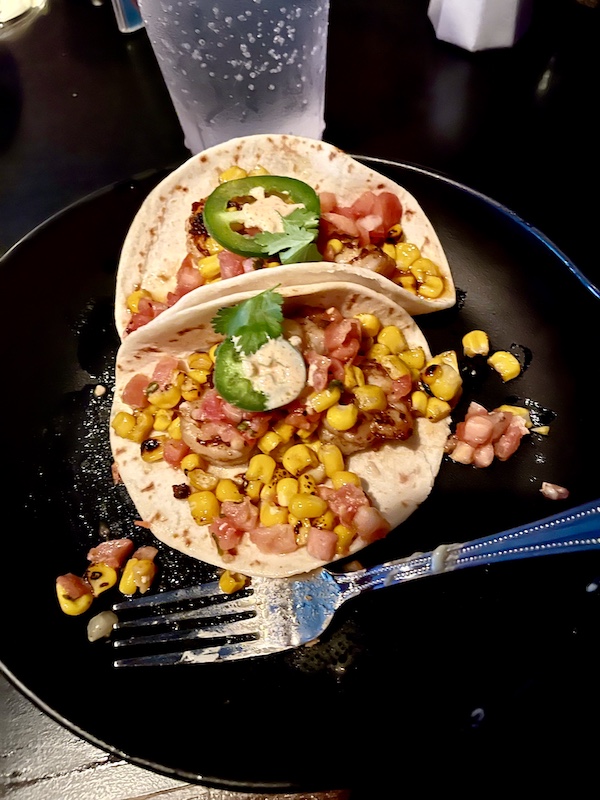 Pair of shrimp filled tacos on a black plate with a fork across the front edge at Basket lined with deli paper and filled with seasoned crinkle fries at Chickie's and Pete's Atlantic City