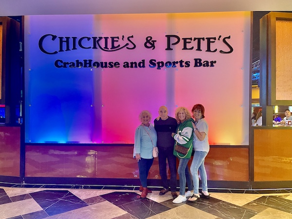 Basket lined with deli paper and filled with seasoned crinkle fries at Chickie's and Pete's Atlantic City's colorful entry wall was a great backdrop for 3 women and a man.