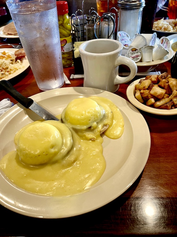 Beige plate topped with two poached eggs covered with lots of Hollandaise sauce and mug of coffee. At Jimmy's Family Restaurant Easley SC this also came with a dish of diced hash browns.
