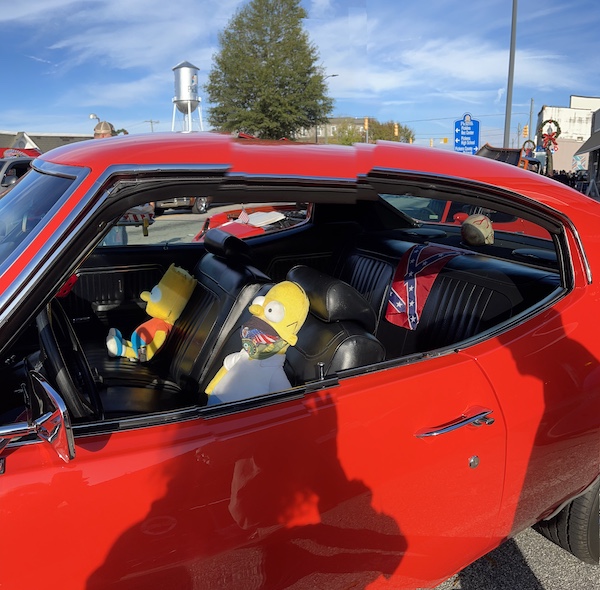 Red car with Simpson dolls in the front seats at the Downtown Pickens Car Show