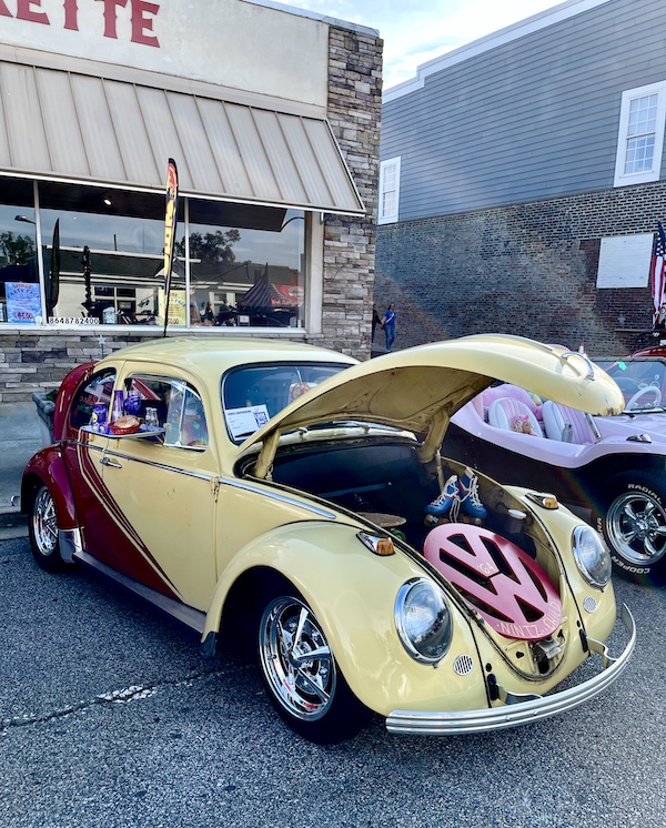Pale yellow VW Beetle with hood up showing a large pink VW logo at the Downtown Pickens Car Show