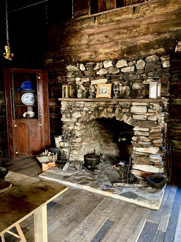 Large stone fireplace for cooking in a log home.