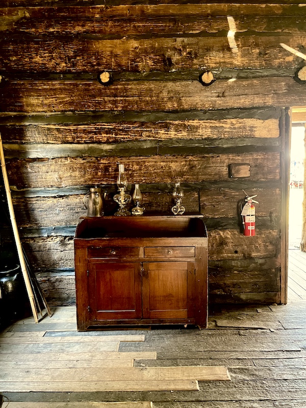 Brass oil lamps sit atop an old wood sideboard in a log house.