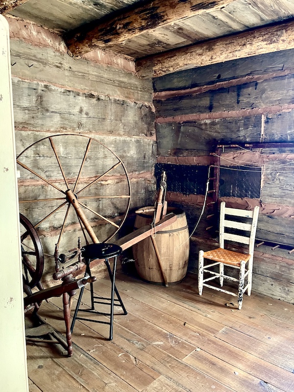 Old spinning wheel and ladder back chair in a log room at the Hagood Mill Native American Celebration