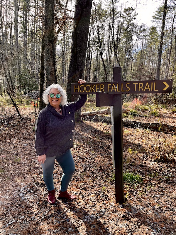 Me, standing by a brown wood sign for Hooker Falls Trail because I'm Happily Back to Writing!