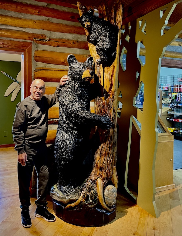Steve standing next to a wood carving of a mama and baby bear at the State Park Visitors Center. Happily Back to Writing!