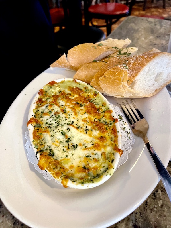 Oval gratin dish filled with shrimp, crab, spinach and artichoke dip with bread slices. French Quarter Girls Lunch appetizer.