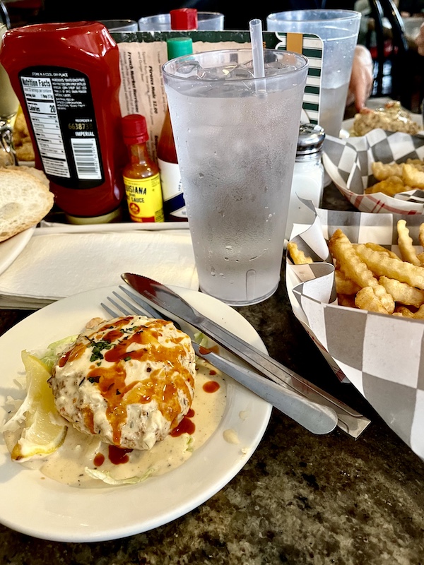 Table full of food including plates with crab cakes and dishes of French Fries, enjoyed at our French Quarter Girls Lunch
