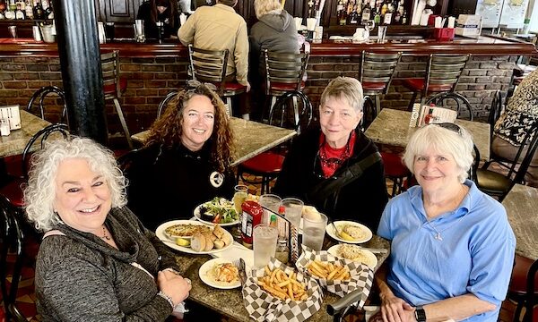 Four women at at restaurant seated at a round table covered with plates of food. It was our French Quarter Girls Lunch.