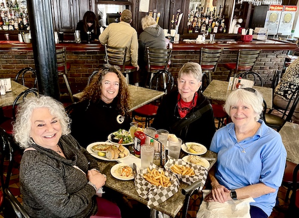 Four women at at restaurant seated at a round table covered with plates of food. It was our French Quarter Girls Lunch.