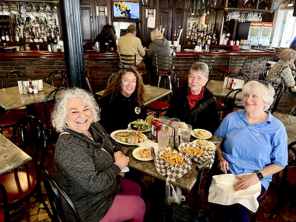 Four women at at restaurant seated at a round table covered with plates of food. It was our French Quarter Girls Lunch.
