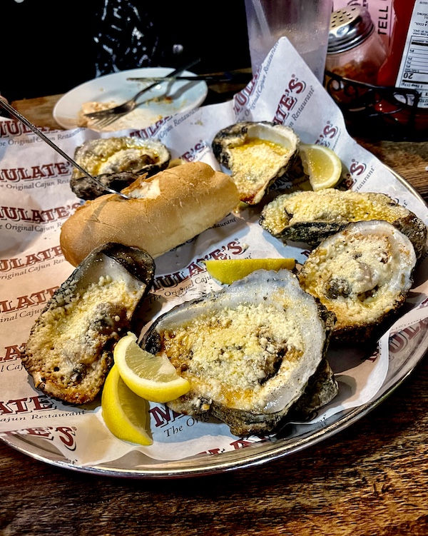 Large platter topped with printed paper and grilled oysters on half shell. At Mulate's the Original Cajun Restaurant it's served with a loaf of bread